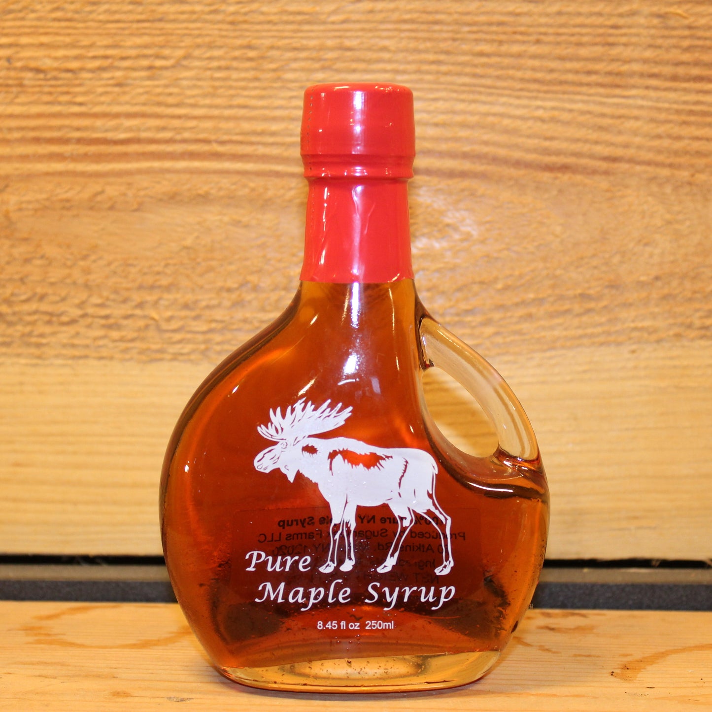 Bottle of pure maple syrup with a red cap on a wooden background with a moose printed on the bottle.